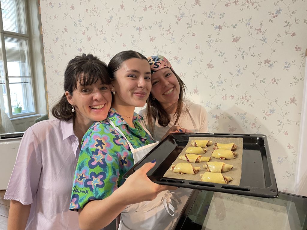Three women putting homemade rugelach pastries into the oven during a Jewish cooking class in Budapest