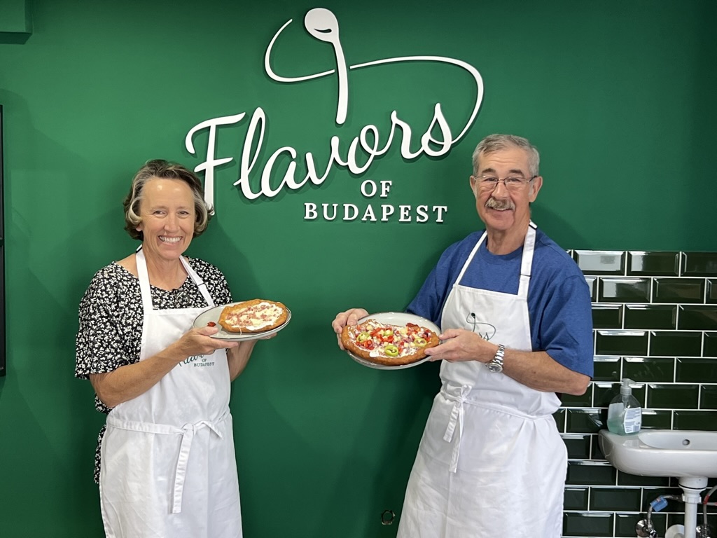 Smiling guests proudly showing their homemade Hungarian Langos topped with delicious ingredients during a cooking class at Flavors of Budapest Opera